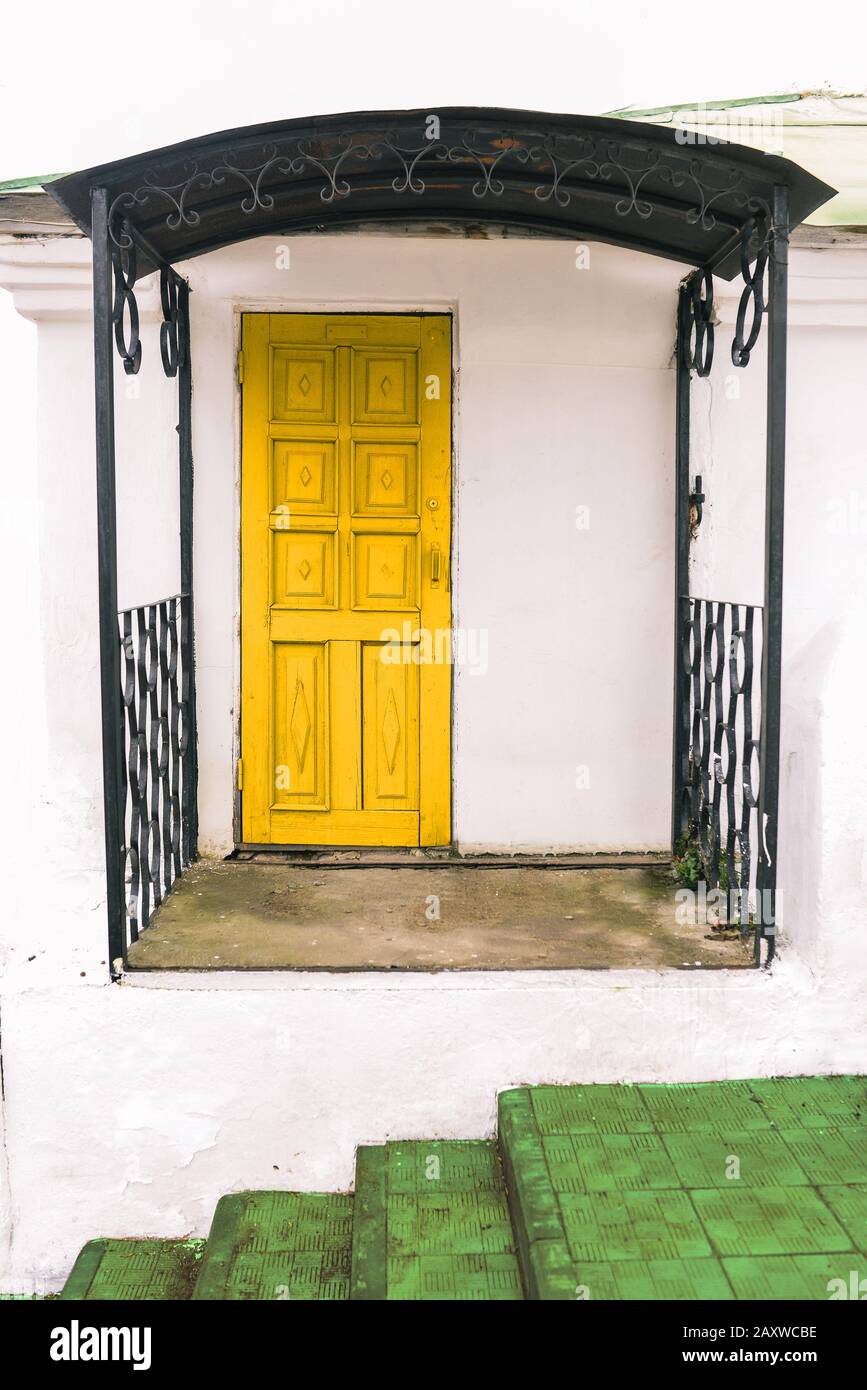 Die Fassade eines kleinen Hauses mit weißen Wänden, einer gelben Tür und einer grünen Treppe. Stadtraum, Architektur. Stockfoto