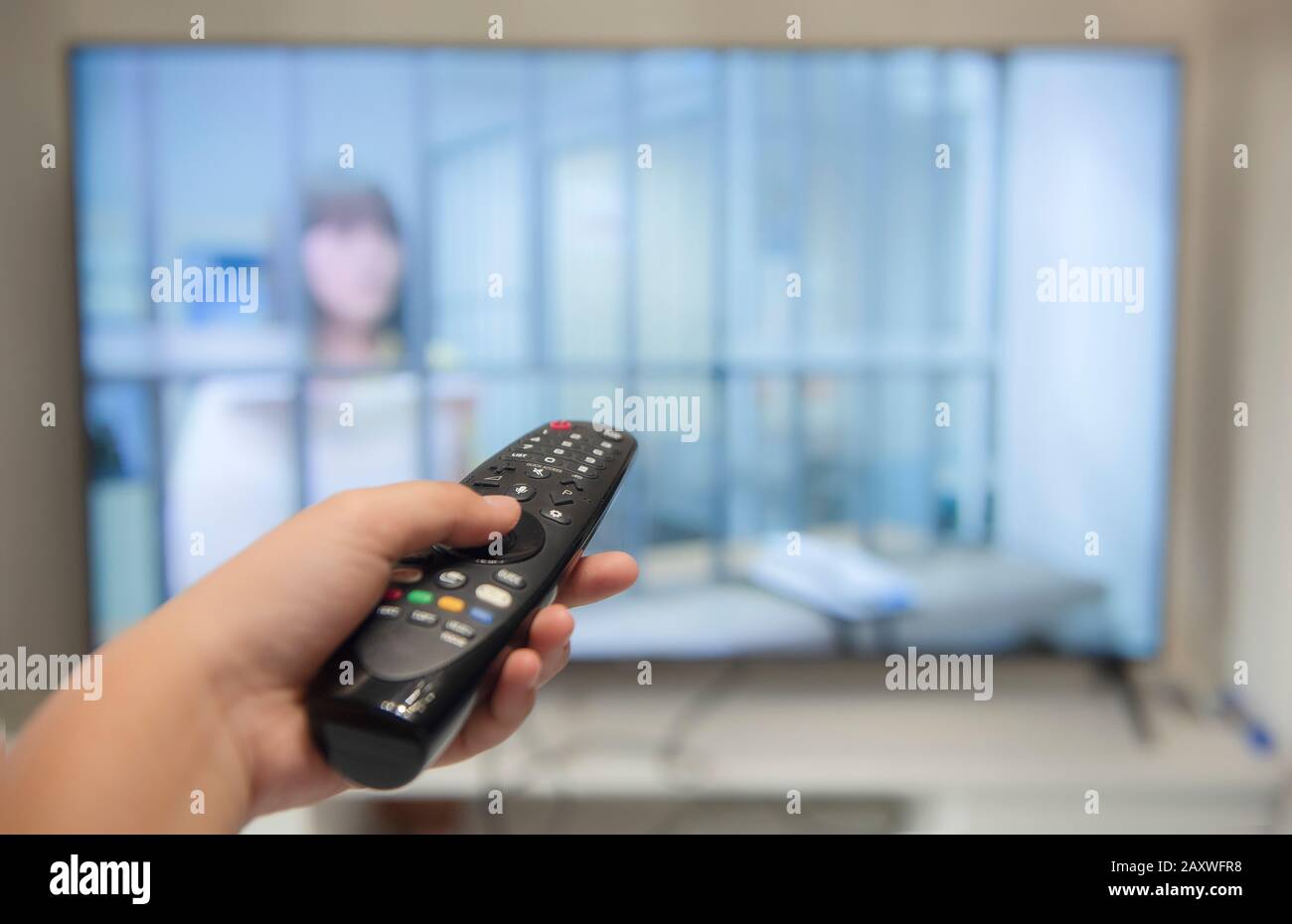 Halten Sie die Fernbedienung des Fernsehers mit einem Fernseher im Hintergrund. Selective Focus Stockfoto