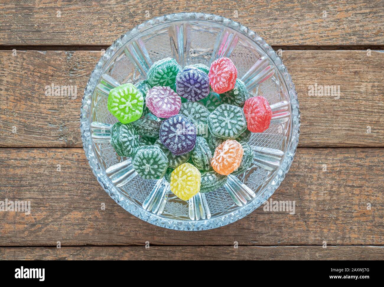 Bunte Süßigkeiten mit Fruchtgeschmack in einer Kristallschale auf einem Holztisch Stockfoto
