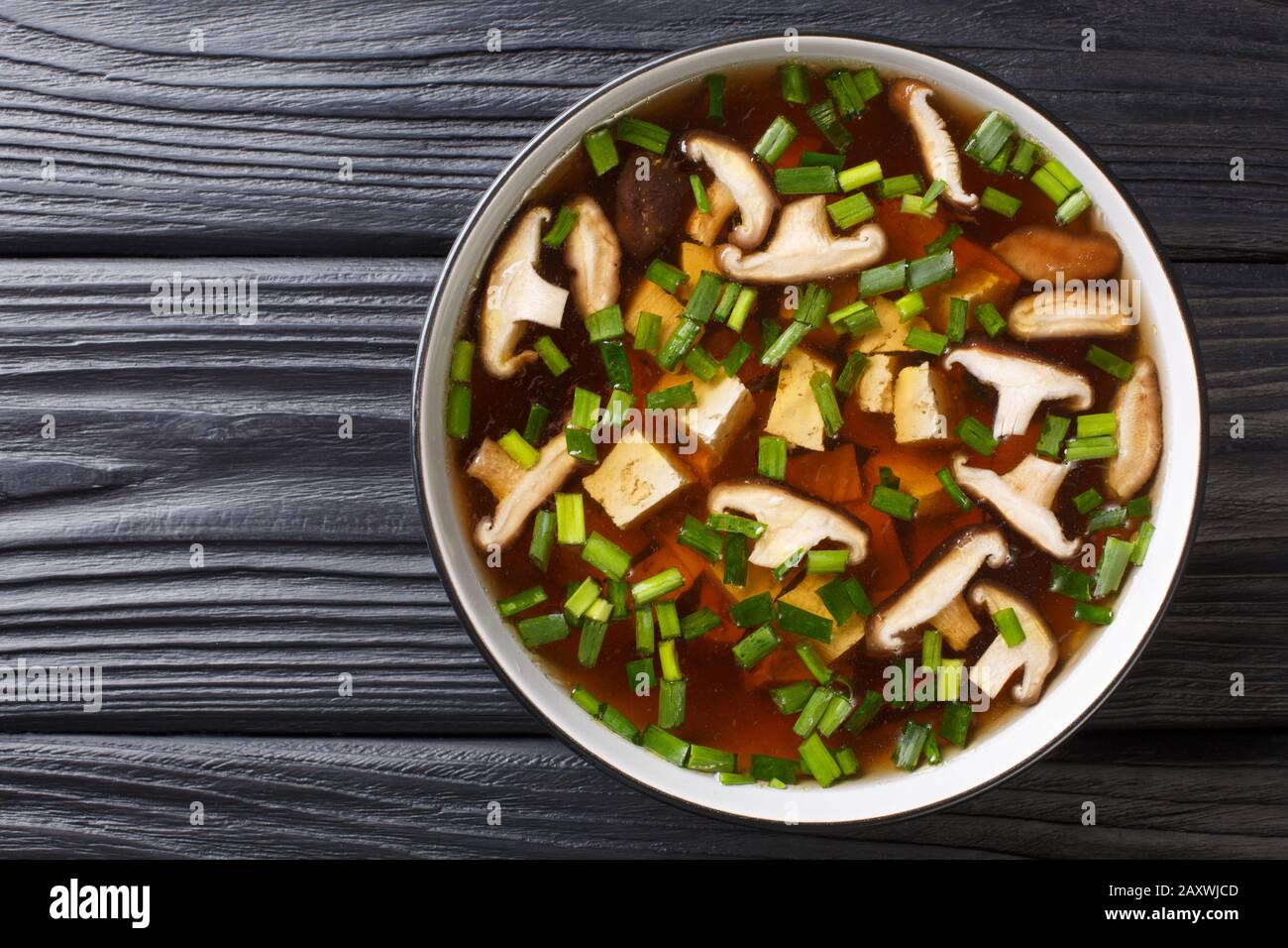 Asiatische Suppe mit Shiitake-Pilzen, Tofu-Käse und grünen Zwiebeln in einer Schüssel auf dem Tisch. Horizontale Draufsicht von oben Stockfoto