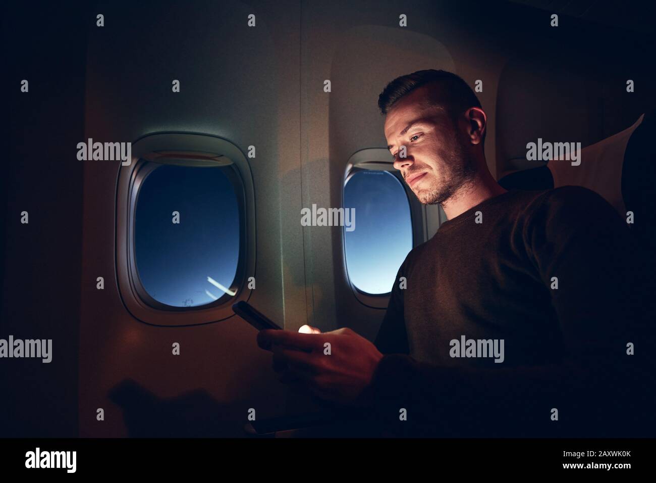 Junger Mann mit Handy im Flugzeug. Internetverbindung während des Flugs. Stockfoto