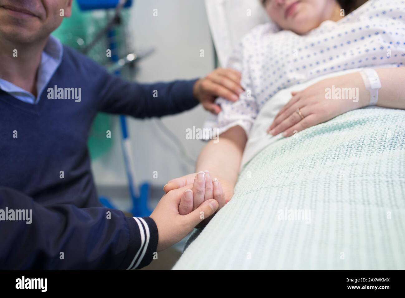 Liebevoller Sohn, der die Hände mit der Mutter hält, die im Krankenbett ruht Stockfoto