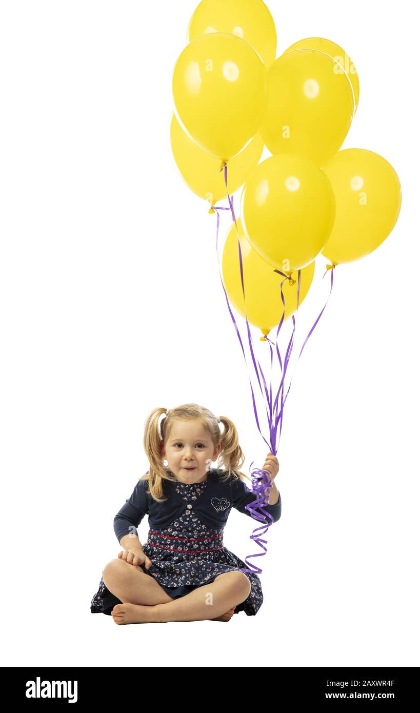 Lächelndes 3-jähriges blondes kaukasisches Mädchen mit Schwänzen hält gelbe Ballons in der Hand. Isoliert auf Weiß. Glücksbegriff und unbeschwertes Kinderho Stockfoto