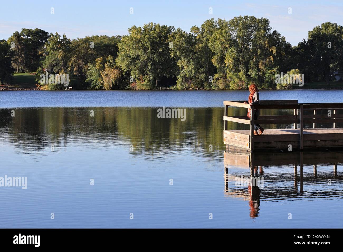 Redhead genießen Sie im Herbst die Lichtreflexe des Sees von einem Dock Stockfoto