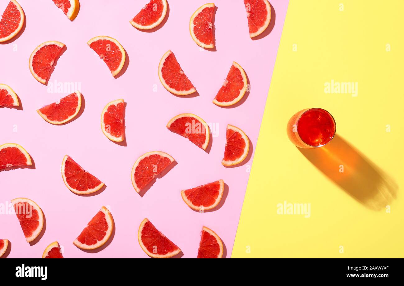 Frische Grapefruitscheiben auf pinkfarbenem Hintergrund und kalte Grapefruitgetränke auf gelbem Hintergrund in der Sommersonne. Bicolor Hintergrund und saftige Grapefruit. Stockfoto