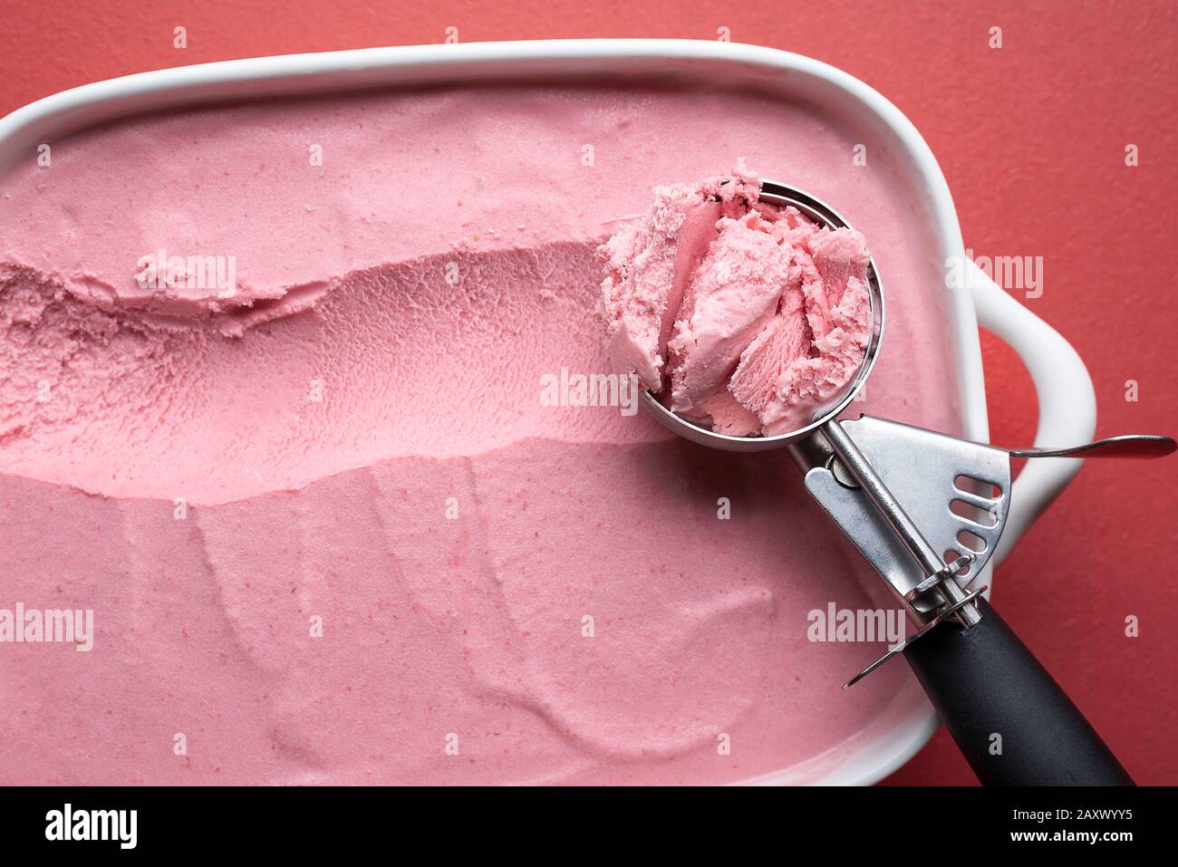 Schaufel mit Himbeereis in Nahaufnahme auf einem roten Tisch. Blick auf hausgemachte Beeren Eiscreme. Frisches Sommerdessert. Details zu rotem Eis. Stockfoto