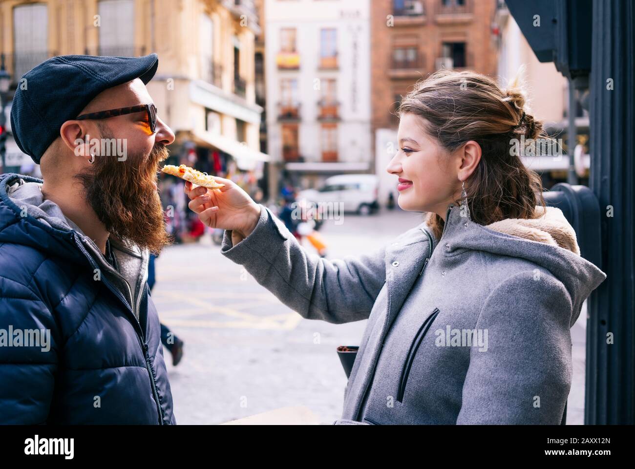 Ein glückliches blondes kaukasisches Mädchen gibt einem Kerl mit Bart und Brille auf einer Straße in der Stadt eine Pizza Stockfoto