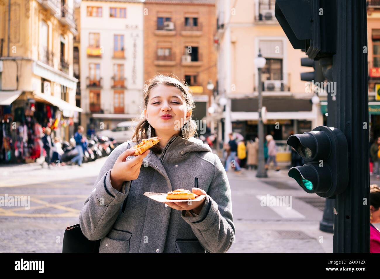 Ein glückliches blondes kaukasisches Mädchen isst Pizza auf einer Straße in der Stadt Stockfoto