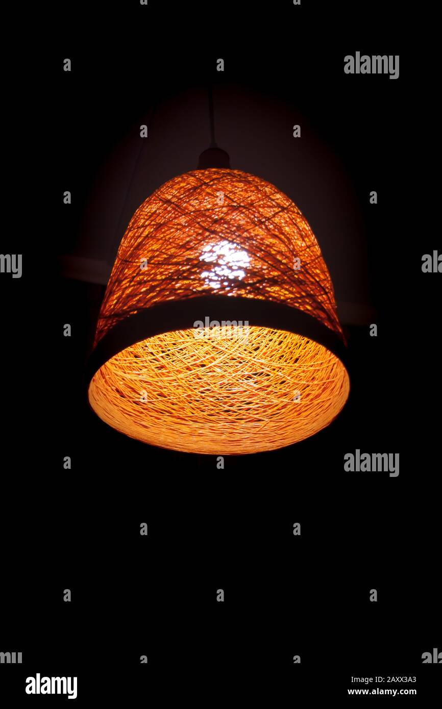 Ein orangefarbener Lampenschirm im Retro-Design mit einer Glühlampe im Holzstil auf dunklem Hintergrund. Detail des Innenraums. Leicht. Konzeptionelles vertikales Foto. Stockfoto