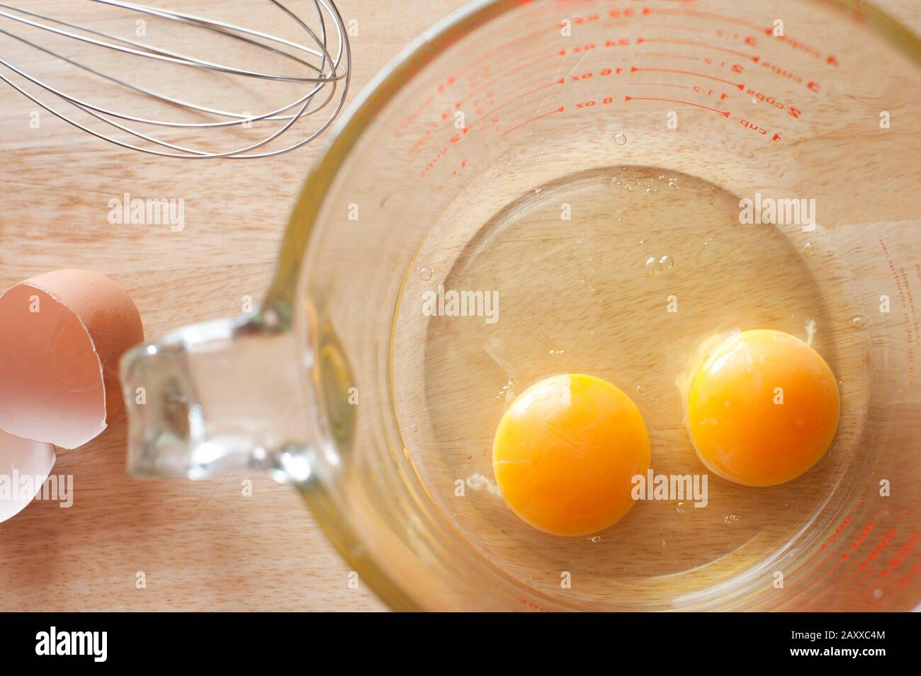 Blick über die Decke von zwei gesunden gelben Eigelb, die in den Boden einer durchsichtigen Messkanne auf einem Küchentisch gebrochen sind, um als Frühstück oder verwendet zu werden Stockfoto