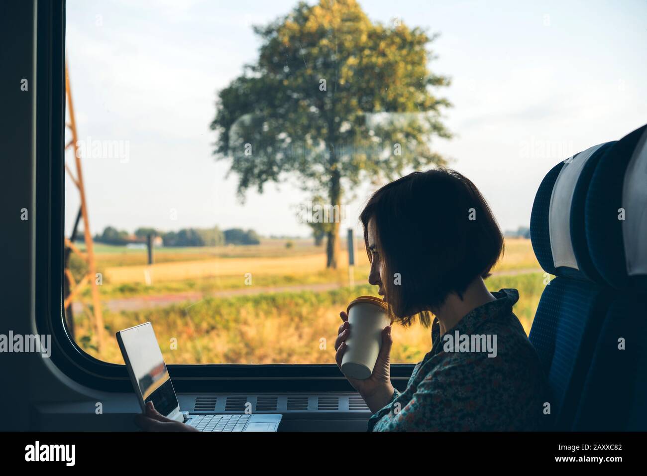 Eine Frau sitzt am Fenster einer S-Bahn mit einem Laptop und Kaffee Tasse Stockfoto
