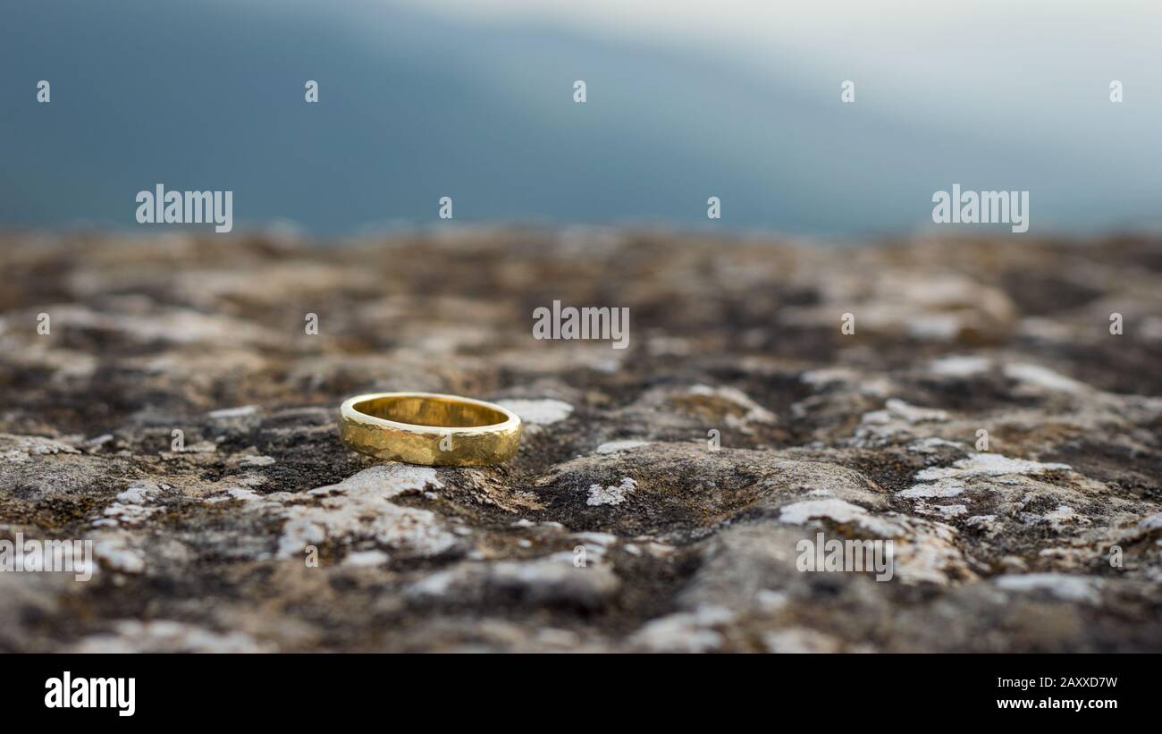 Goldener Hochzeitsring auf einem Stein mit Blick auf den Himmel im Hintergrund Stockfoto