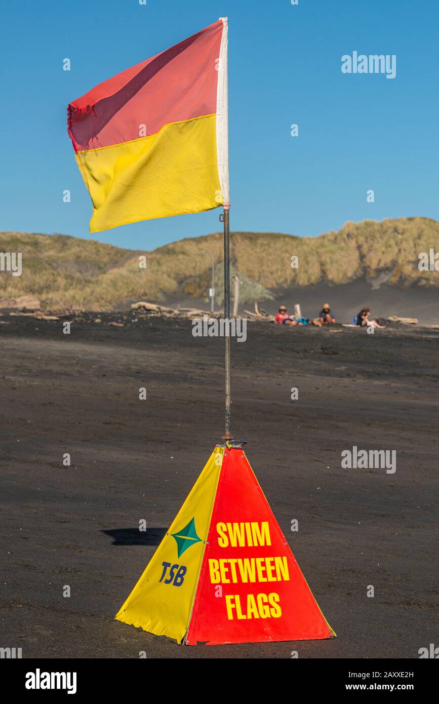 Neuseeländische Surfrettungsfahne und -Markierung im Hochformat, am schwarzen Eisen-Vulkansand des Castlecliff Beach in Whanganui. Stockfoto