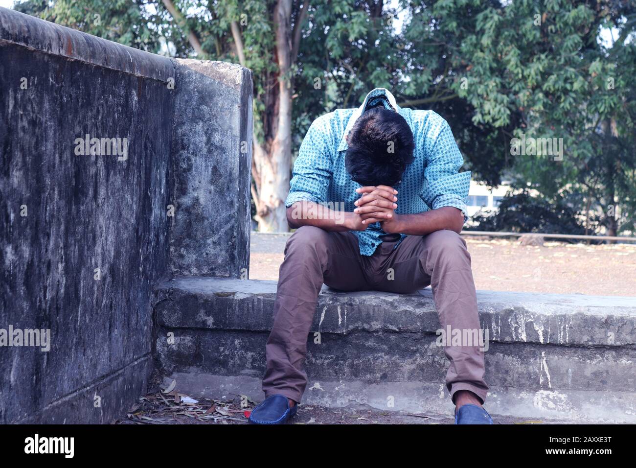 Depressiver Teenager, der allein an der Wand im Freien sitzt. Unangenehme Schmerzen. Traurig unglücklicher, gutaussehender Mann. Bangladesch und Asien leiden unter einer Depression. Stockfoto