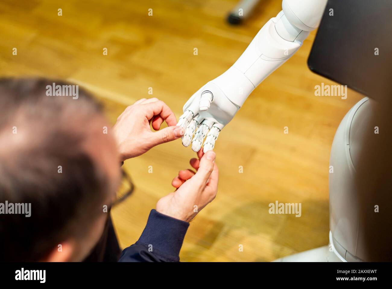 Mann mittleren Alters greift sanft und hält eine weiße Hand eines humanoiden Roboterassistenten, untersucht seinen mechanischen Arm, seine Finger. Künstliche Intelligenz Stockfoto