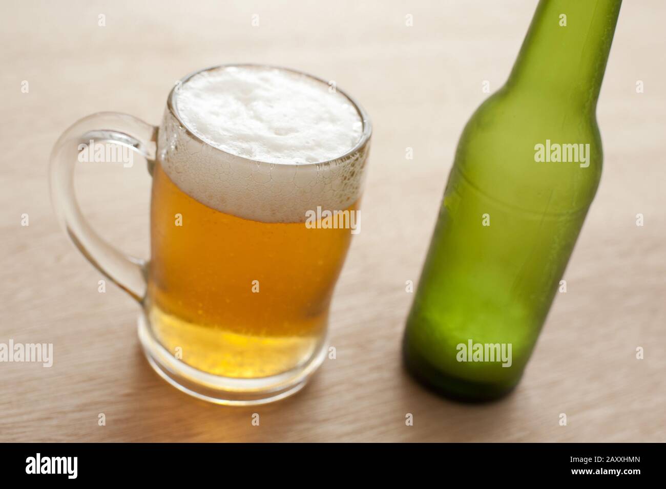 Nahaufnahme des hohen Winkels einer Glaskerde und einer unbeschrifteten grünen Flasche kaltem Bier auf einer Holzbar Stockfoto