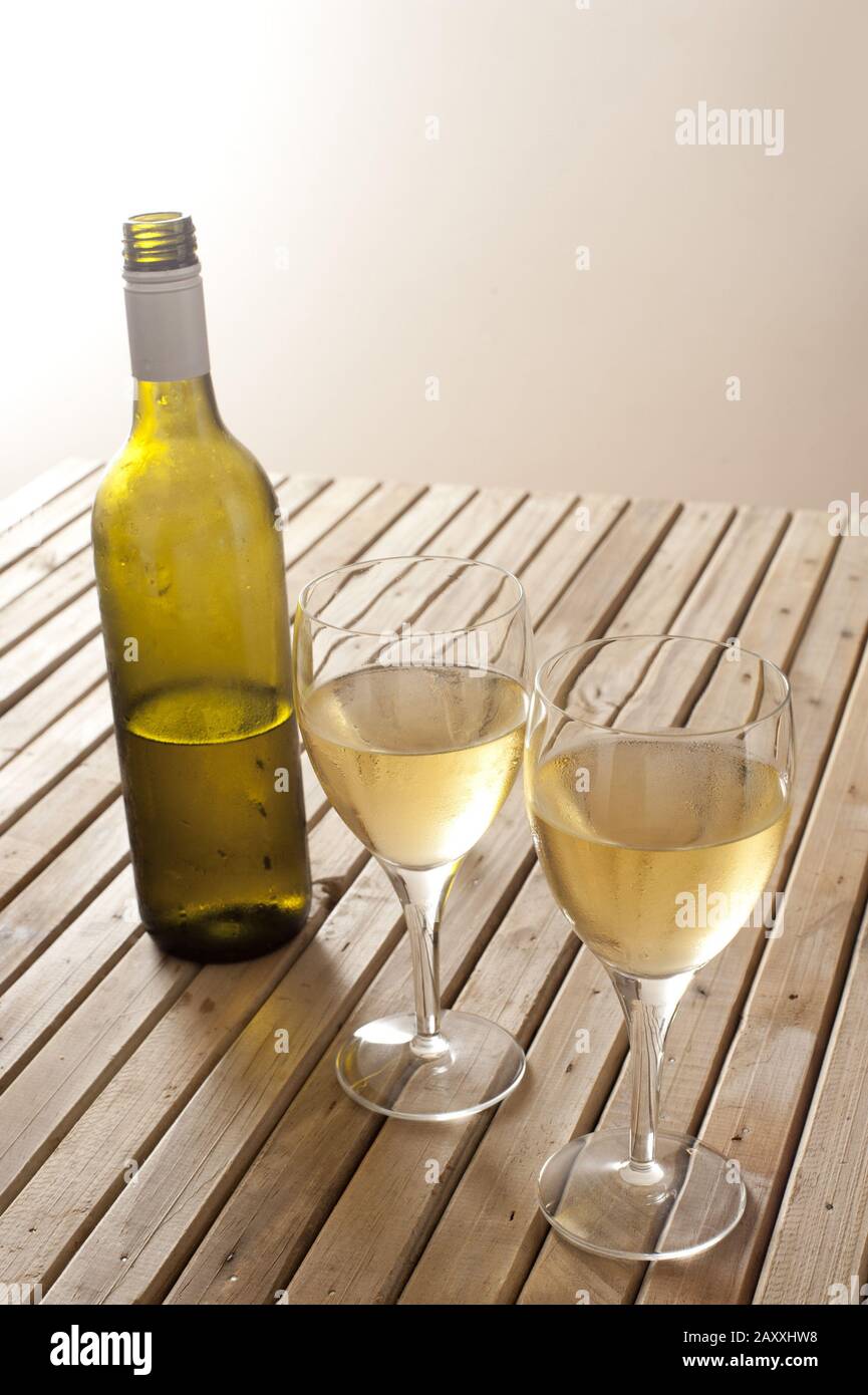 Öffnen Sie eine unbeschriftete Weißweinflasche mit zwei vollen Gläsern Wein auf einem Holztisch mit Holzklöscherei und Copyspace Stockfoto