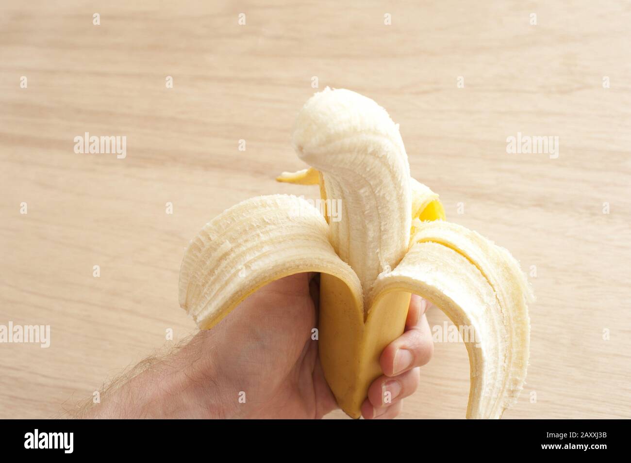 Ungeborchte Banane in der Hand des Menschen vor Holzhintergrund Stockfoto