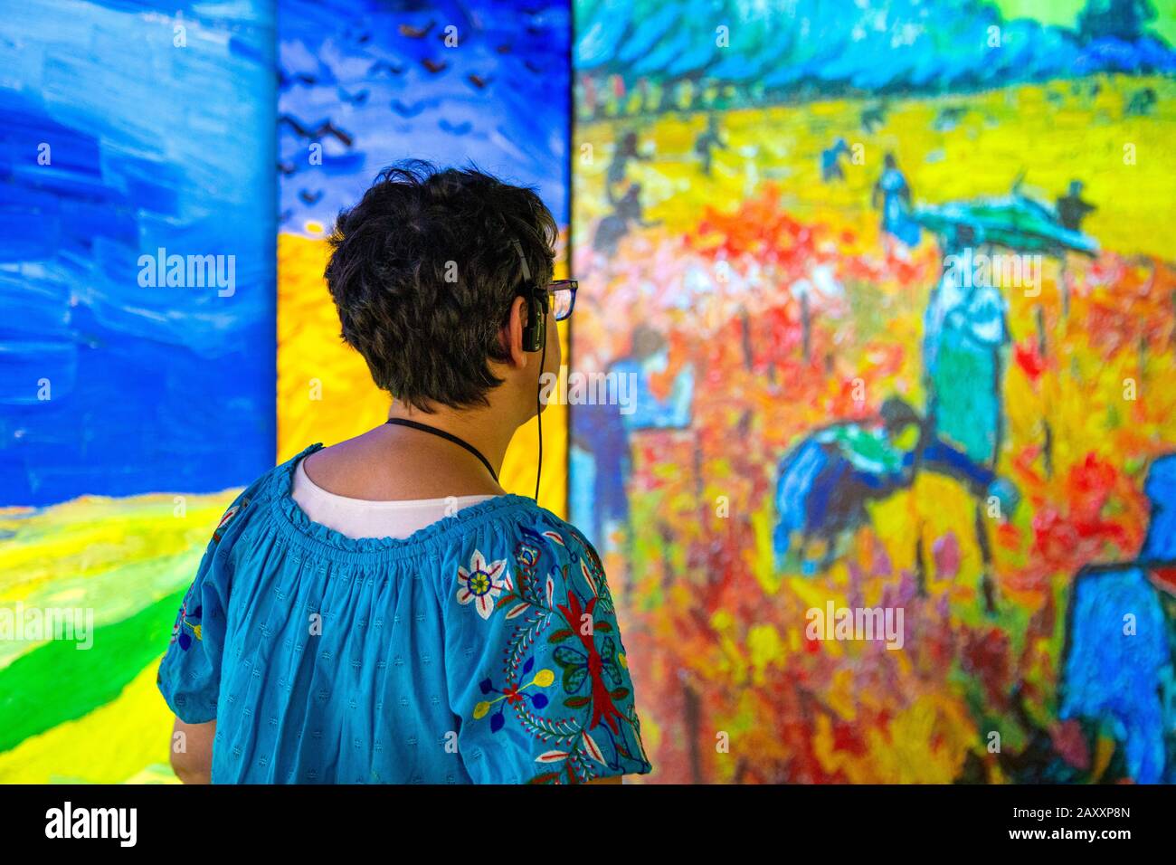 Frau mit Kopfhörern zum hören von Audioguide und Blick auf Gemälde, die auf Wände projiziert werden, Trifft Vincent van Gogh Experience 2020, London, Großbritannien Stockfoto