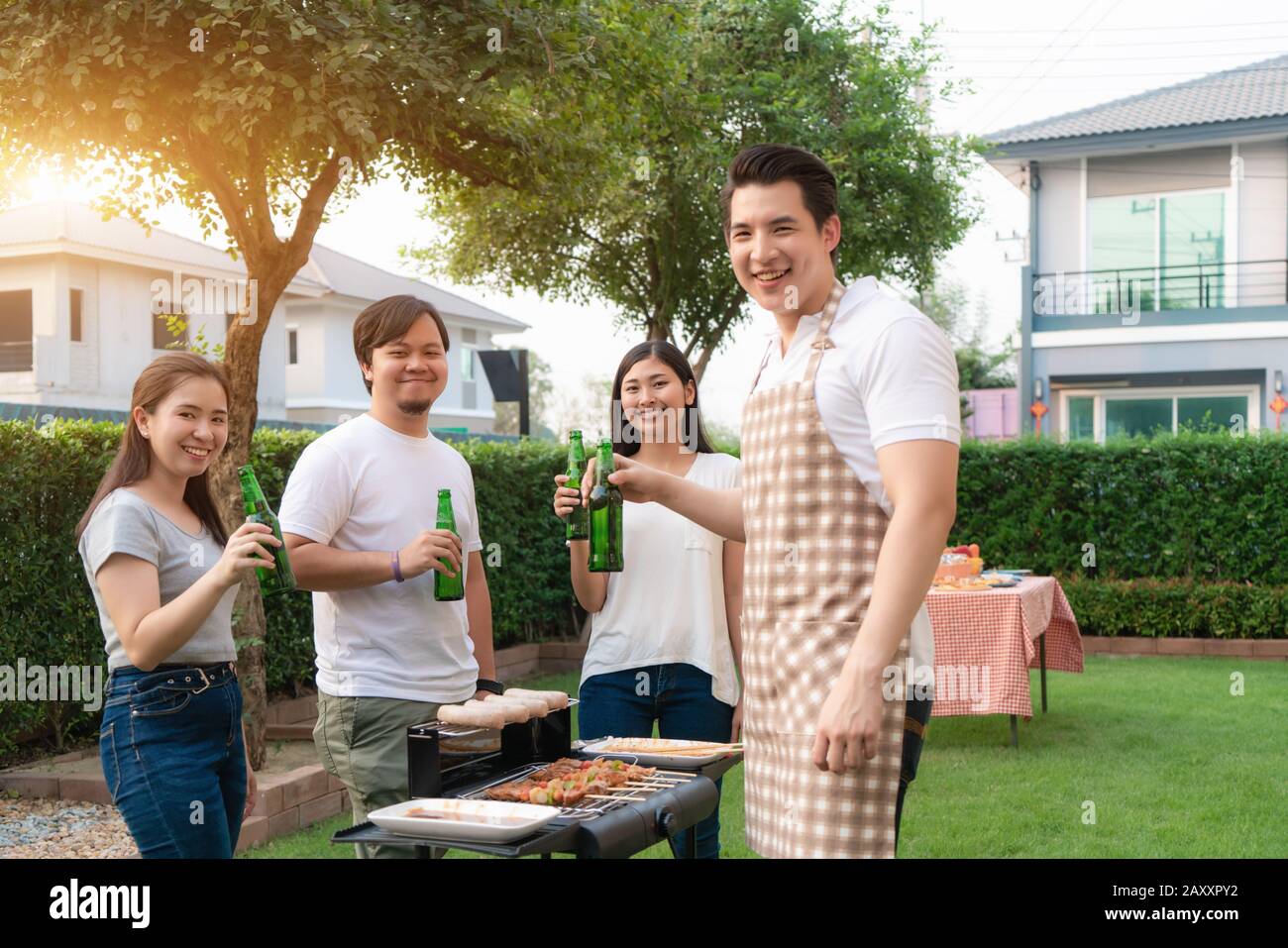 Asiatischer Mann, der grillt und Wurst für eine Gruppe von Freunden kocht, um im Garten zu Hause Party zu essen. Gruppe von Freunden, die Gartengrill la im Freien haben Stockfoto