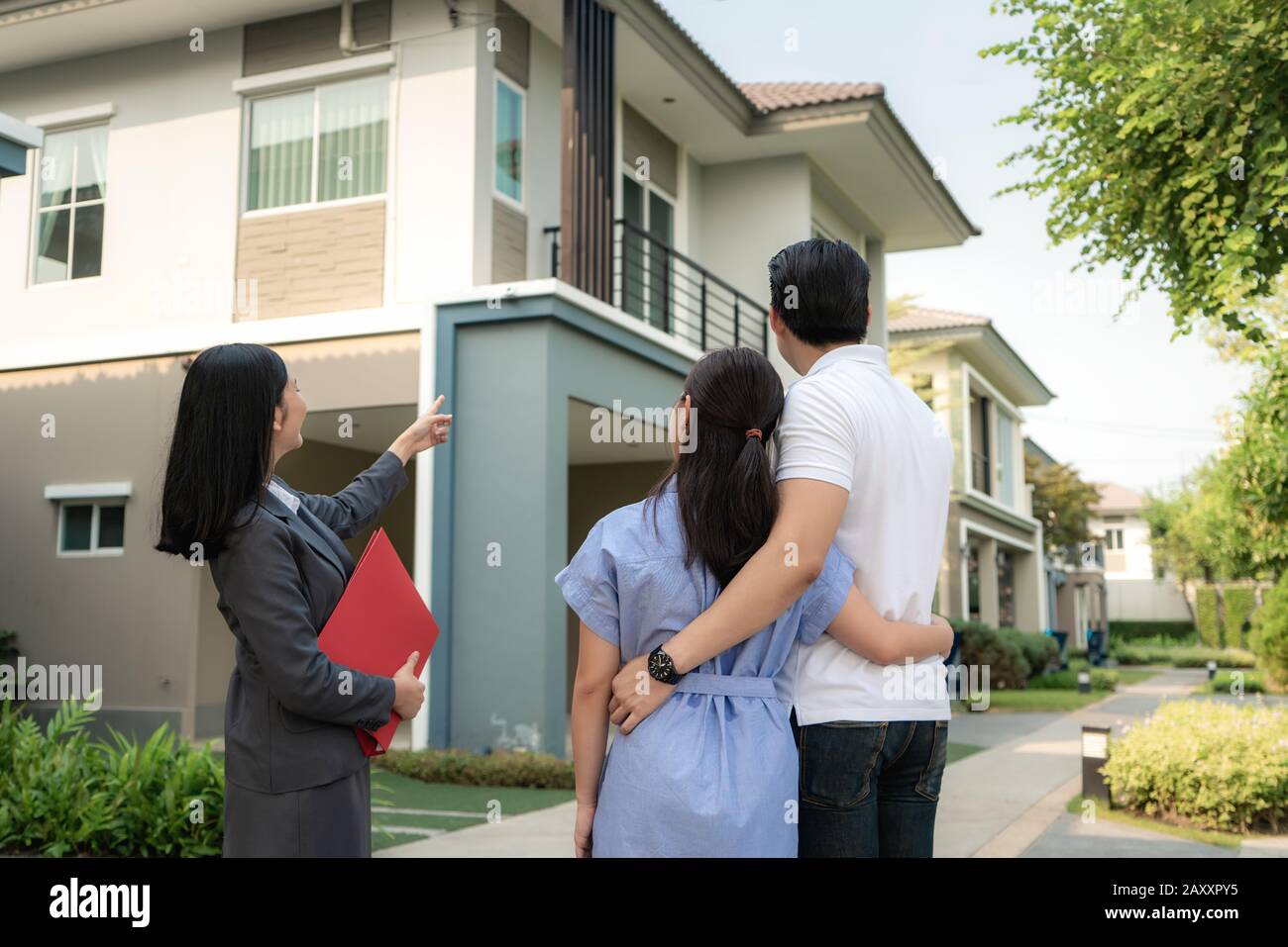 Asian Woman Immobilienmakleragentin, die dem jungen asiatischen Liebespaar, der es sucht und Interesse daran hat, ein Hausprojekt in ihrer Akte ausführlich zeigt. Kaufen Stockfoto
