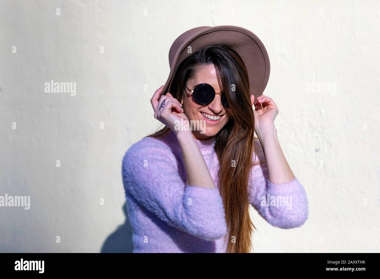 Vorderansicht einer schönen, trendigen jungen Frau, die Sonnenbrille und Hut trägt, die an einem sonnigen Tag auf der Straße steht und sich vor der Kamera stellt Stockfoto