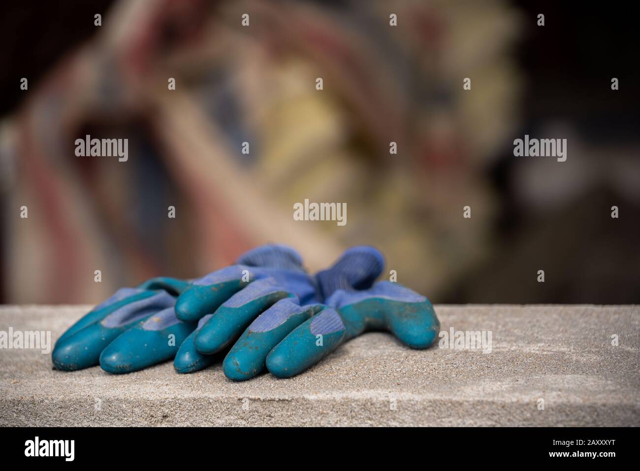 Zwei blaue pvc-Schutzhandschuhe, die vom Bauunternehmer auf der Baustelle verwendet und nach Schichtende an der Steinwand belassen wurden Stockfoto