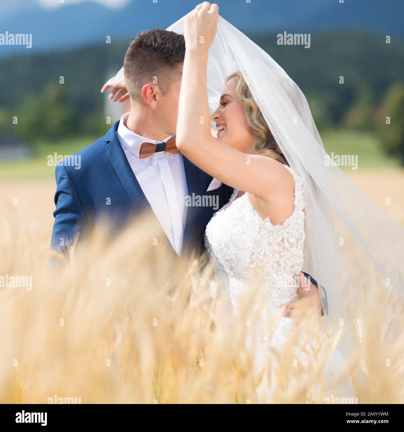 Bräutigam Braut zärtlich umarmt, während der Wind bläst, ihren Schleier in Weizen Feld irgendwo in der slowenischen Landschaft. Stockfoto