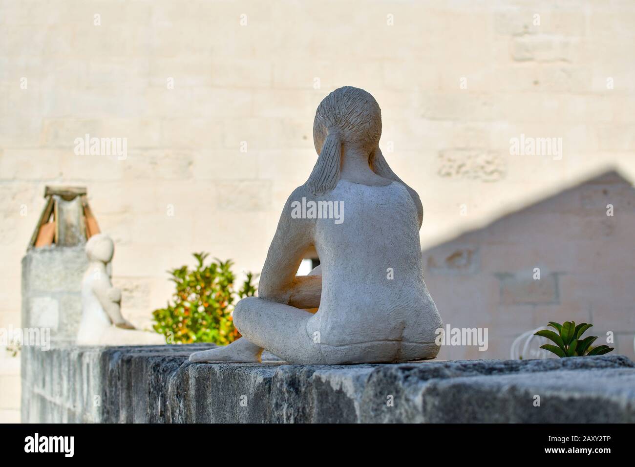 Selektive Fokussierung auf eine moderne Skulptur einer weiblichen Figur, die mit dem Rücken zur Kamera sitzt, während sie einer anderen ähnlichen Skulptur auf einem Dach gegenübersteht. Stockfoto