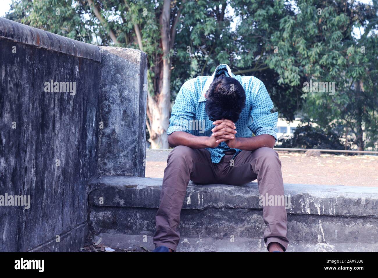 Depressiver Teenager, der allein an der Wand im Freien sitzt. Unangenehme Schmerzen. Traurig unglücklicher, gutaussehender Mann. Bangladesch und Asien leiden unter einer Depression. Stockfoto