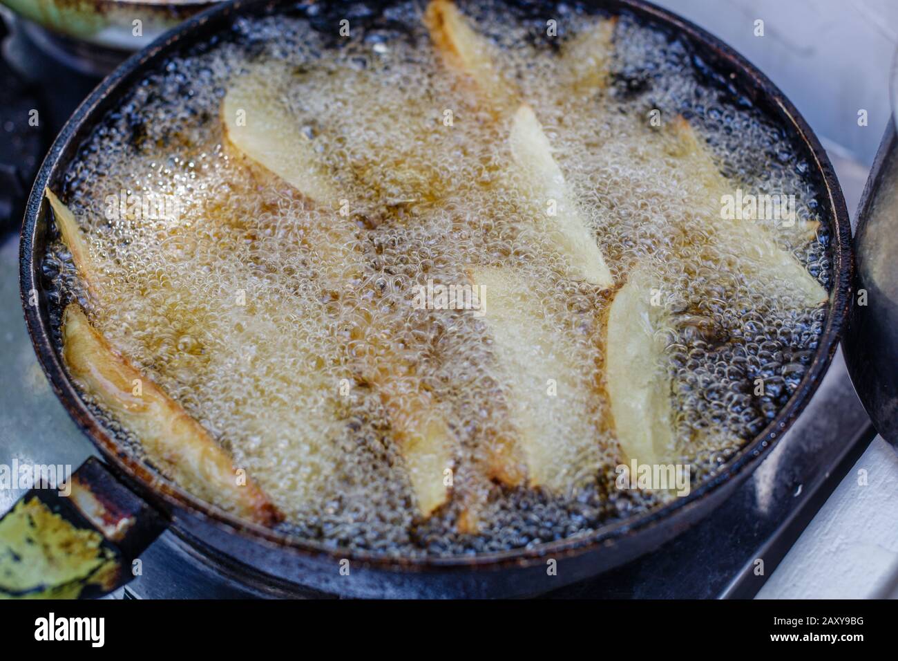Gewürzte Kartoffelkeile, die in heißem Öl auf einer gusseisernen Pfanne braten. Prozess. Stockfoto
