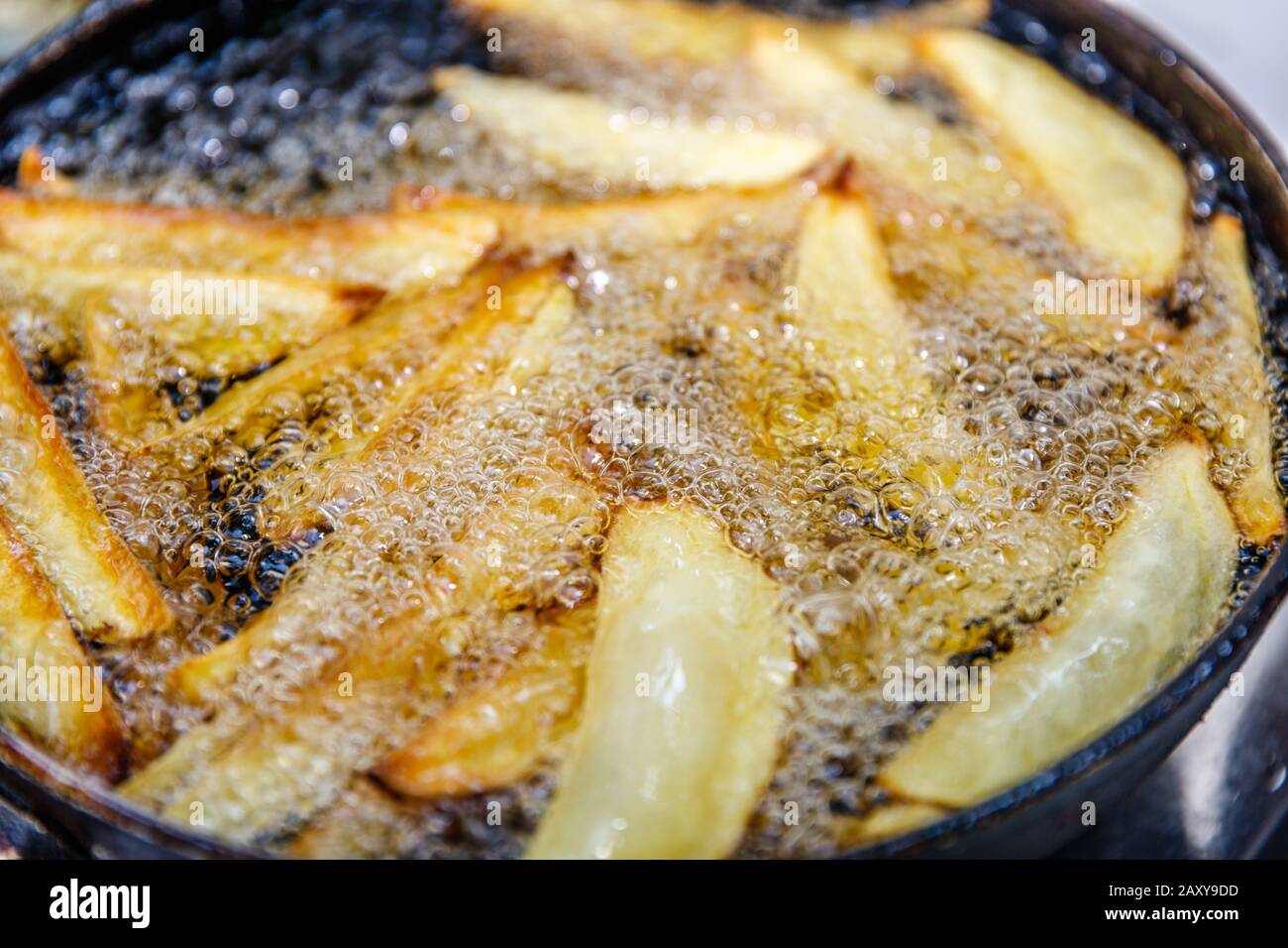 Gewürzte Kartoffelkeile, die in heißem Öl auf einer gusseisernen Pfanne braten. Prozess. Stockfoto