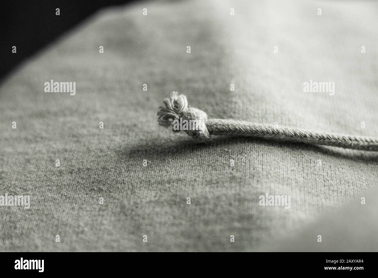 Geknotete Kordelkette auf einem Leicht grau gewebten Textilgewebe, textile Struktur, Nahaufnahme, Makro detailliert Stockfoto