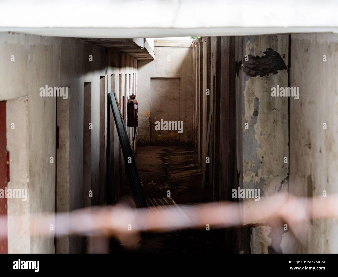 Innenkorridor eines verlassenen Gebäudes mit mehreren Türen, die auf Wohnräume oder Zellen hinweisen, die durch einen Drahtzaun betrachtet werden Stockfoto