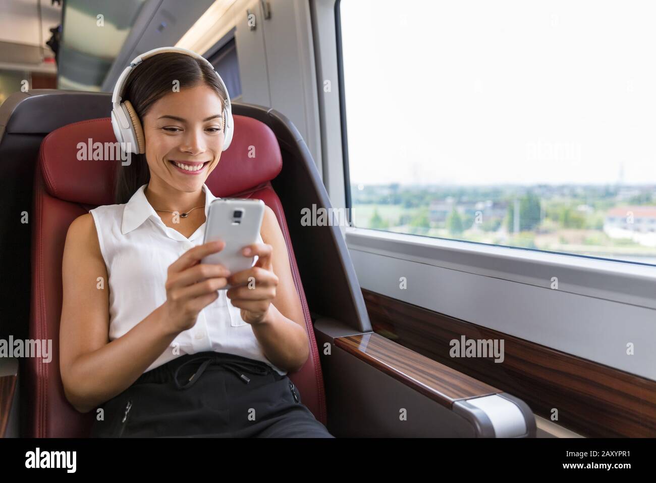 Moderner Lebensstil der Menschen in der Stadt. Junge urbane Frau mit Telefon-App und kabellosen Kopfhörern, um Musik zu hören oder Videospiele online zu spielen. Asiatische Mädchen genießen Zugfahrt auf dem Sitz der Business-Klasse. Stockfoto