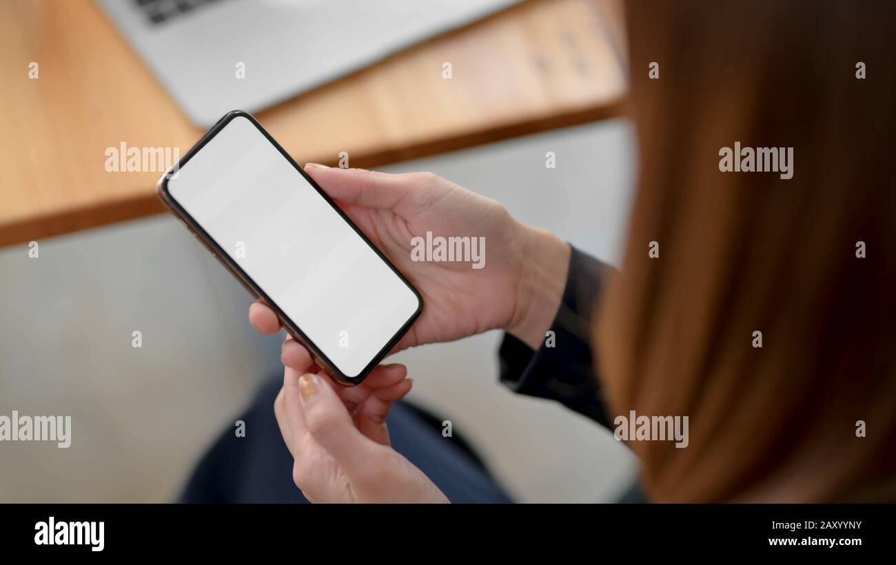 Freigestellte Geschäftsfrau mit leerem Bildschirm-Smartphone mit Laptop auf Holzschreibtisch beim Sitzen am einfachen Arbeitsplatz Stockfoto