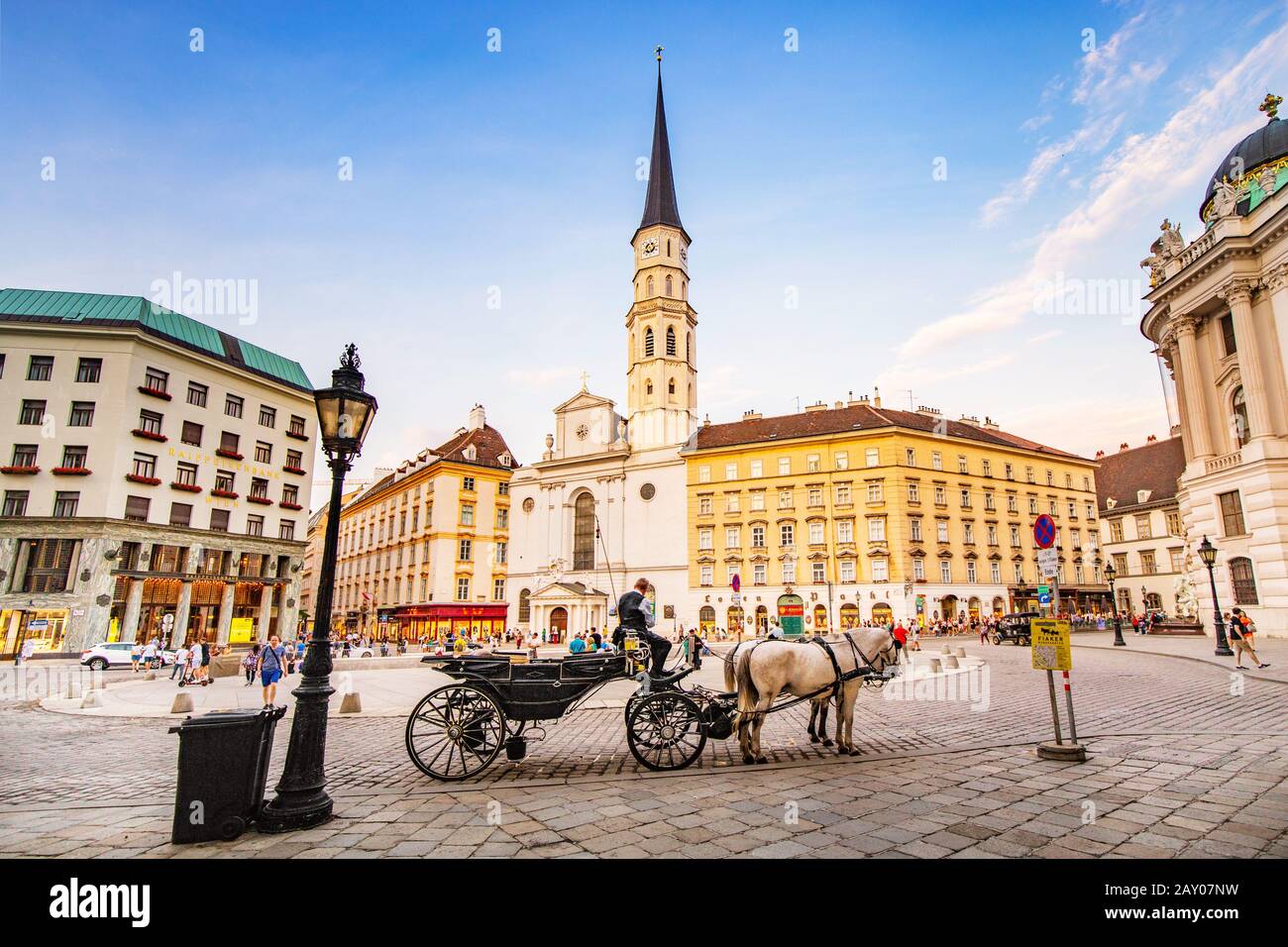 19. Juli 2019, Wien, Österreich: Panoramablick auf die St.-Michael-Kirche auf dem Michaelerplatz mit Pferdetrainer und Touristen Stockfoto