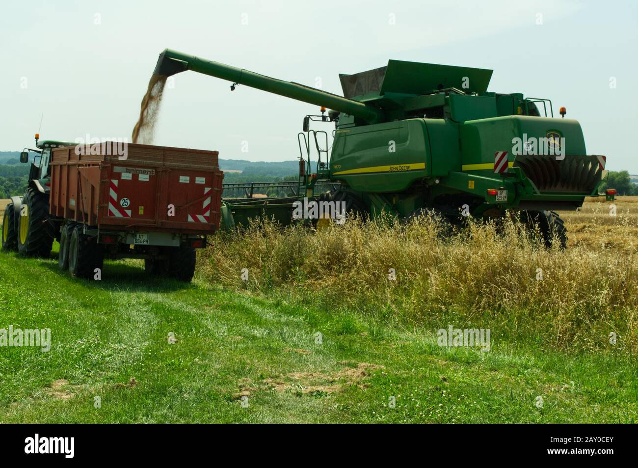 Getreide von einem John Deere T670 Hillmaster Mähdrescher auf einen landwirtschaftlichen Anhänger bringen, während er Weizen in der Nähe von Duras, Lot-et-Garonne, Frankreich erntet. Stockfoto