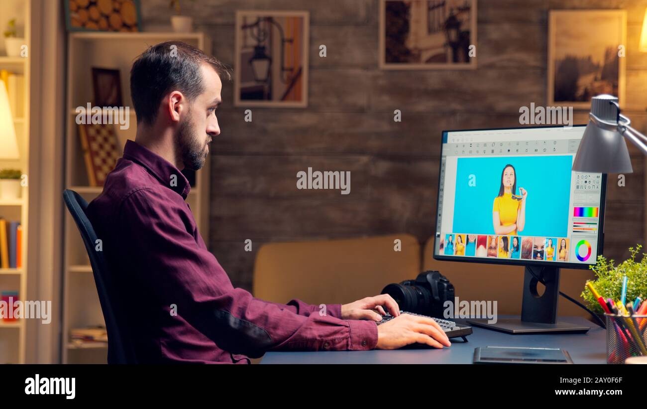 Männlicher Fotograf verwendet Tablet, um Fotos auf dem Computer im Home Office zu retuschieren. Künstler, der nachts arbeitet. Stockfoto