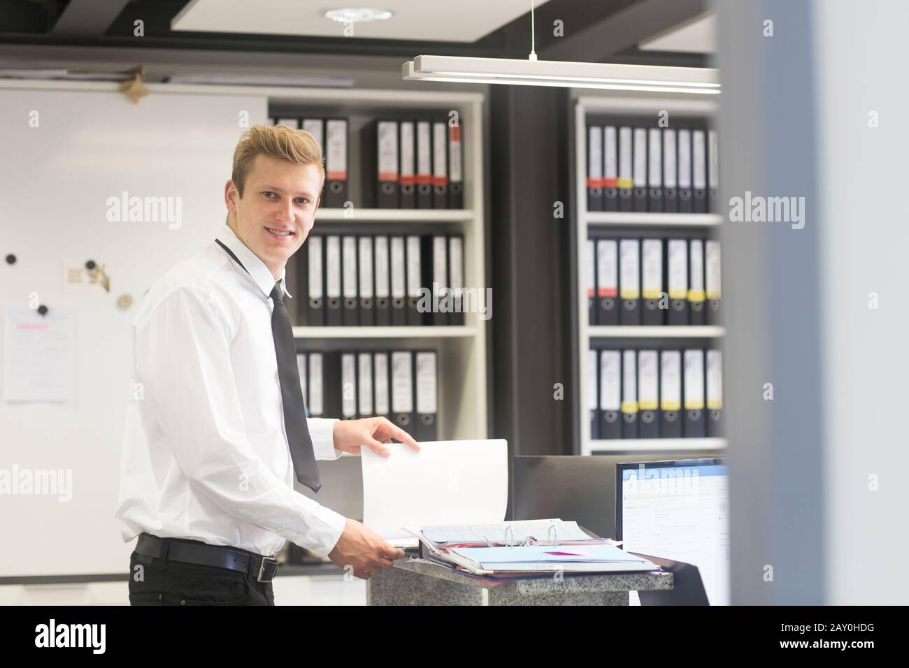 Lächelnder Verkäufer steht im Büro eines Ladens und betrachtet eine Broschüre, Deutschland Stockfoto