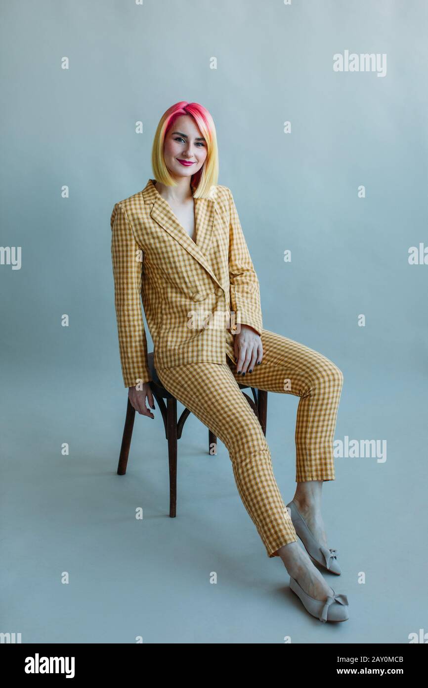 Porträt eines coolen Mädchens mit gefärbtem Haar in einem Anzug, der auf einem Stuhl sitzt Stockfoto