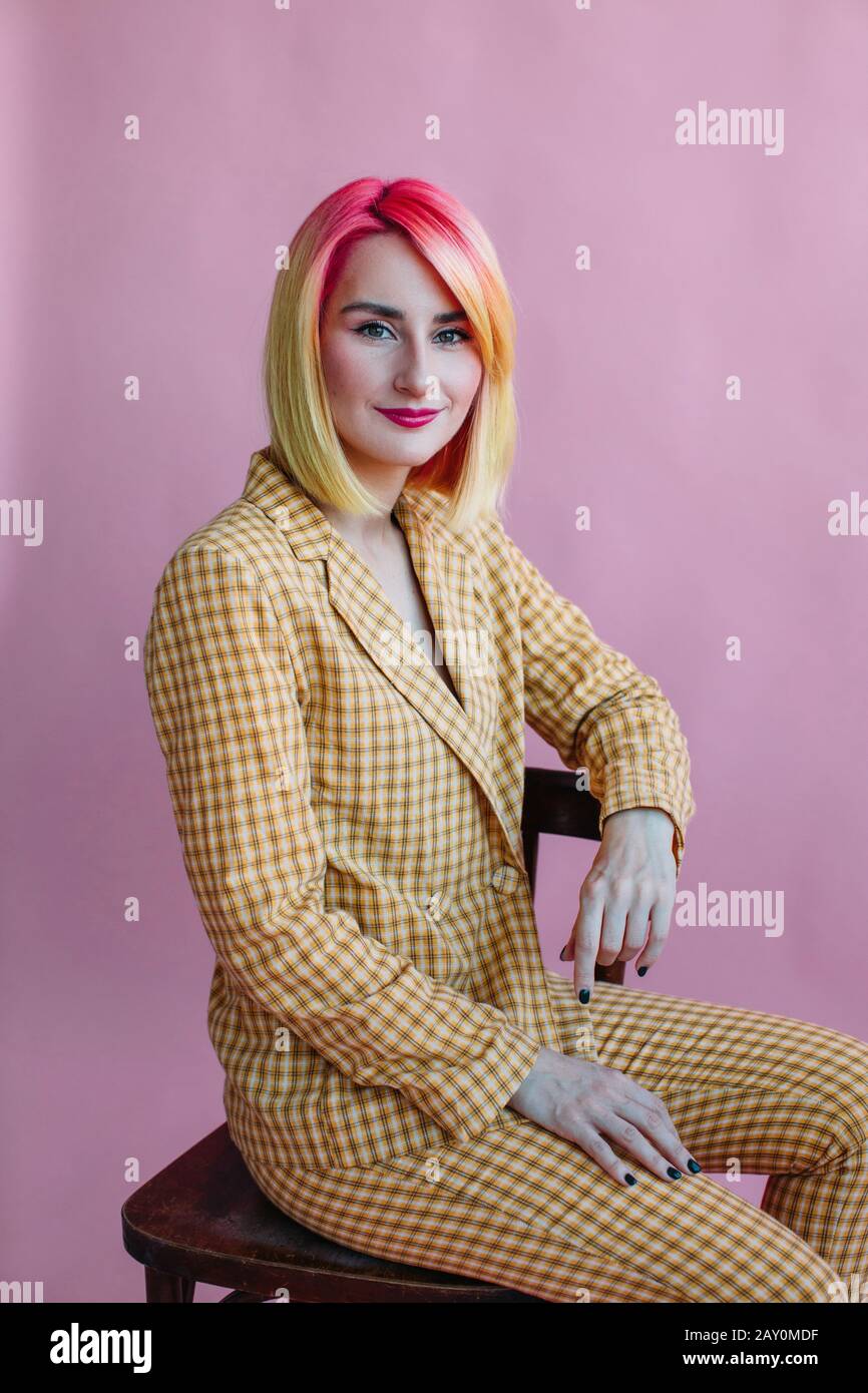 Porträt eines coolen Mädchens mit gefärbtem Haar in einem Anzug, der auf einem Stuhl sitzt Stockfoto