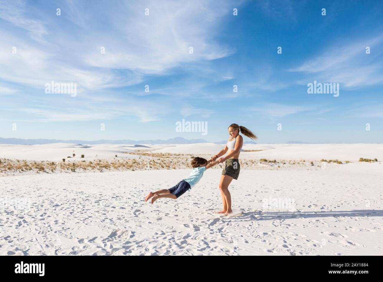 Teenager-Mädchen, die ihren 6 Jahre alten Bruder in Sand schwangen, White Sands Nat'l Monument, NM Stockfoto