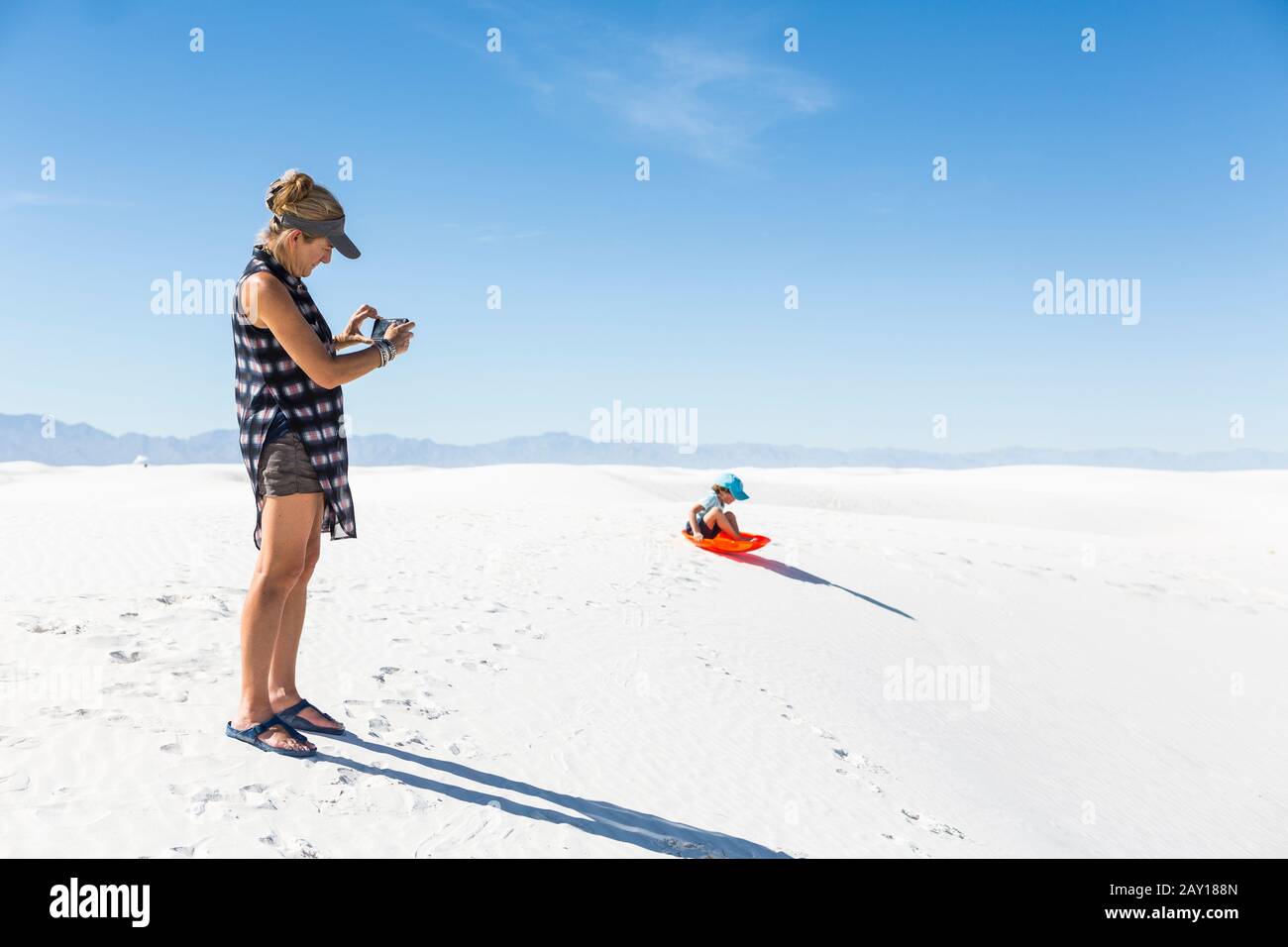 Mutter, die sich auf Sanddünen mit dem Rodeln eines Sohnes fotografieren kann Stockfoto