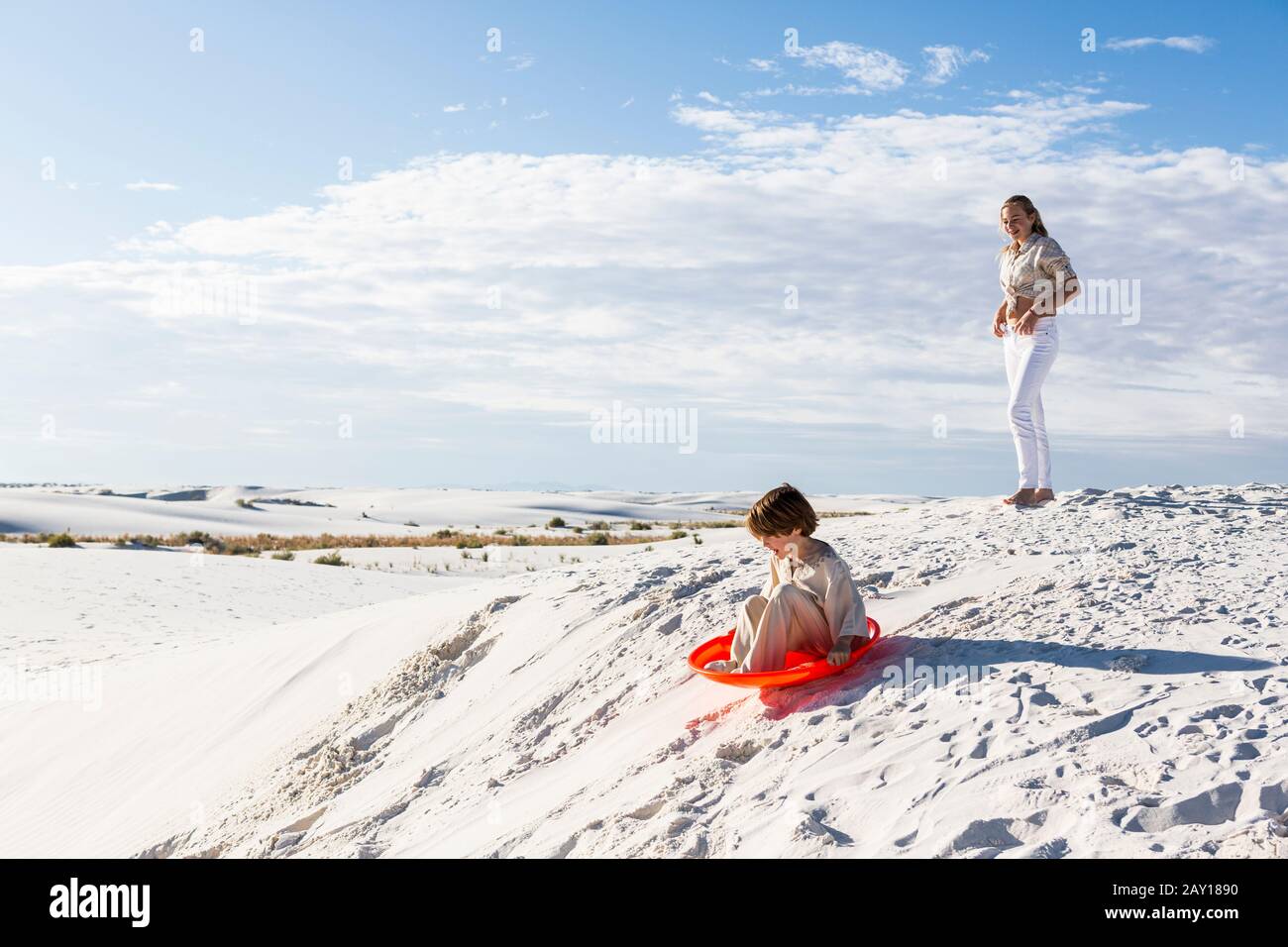 Kinder, die in Sanddünen spielen, eine auf einem orangefarbenen Schlitten. Stockfoto
