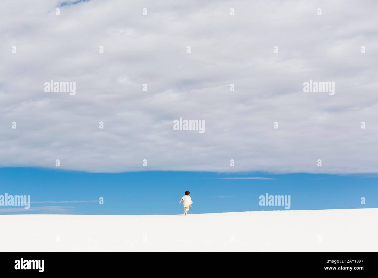 6 Jahre alter Junge, der in weißen Sanddünen spazieren ging, ein Streifen blauer Himmel am Horizont und eine dicke Wolke. Stockfoto