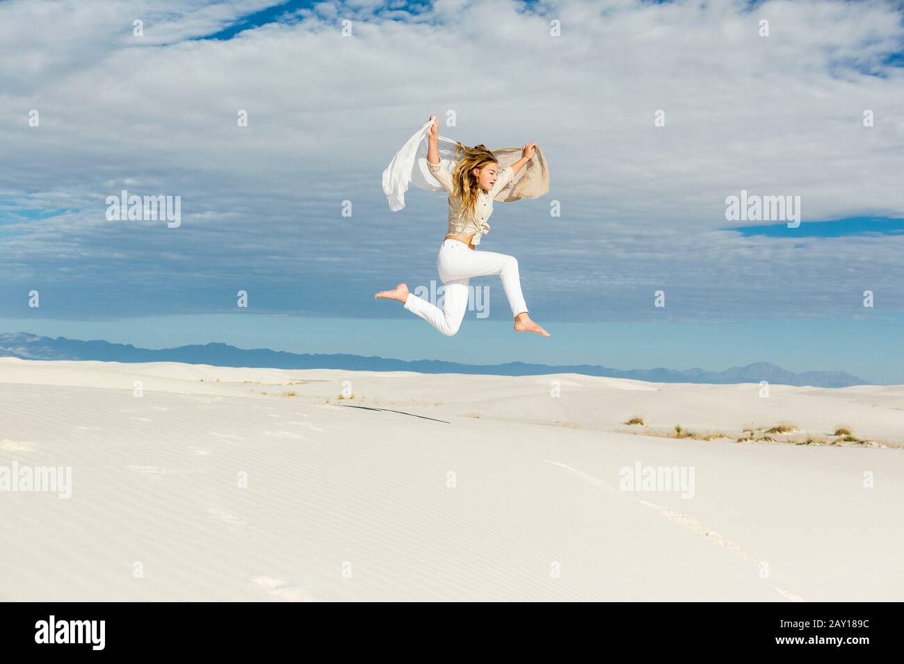 13 Jahre altes Mädchen tanzt und sprang mitten in der Luft auf dem Freigelände auf weißen Sanddünen Stockfoto
