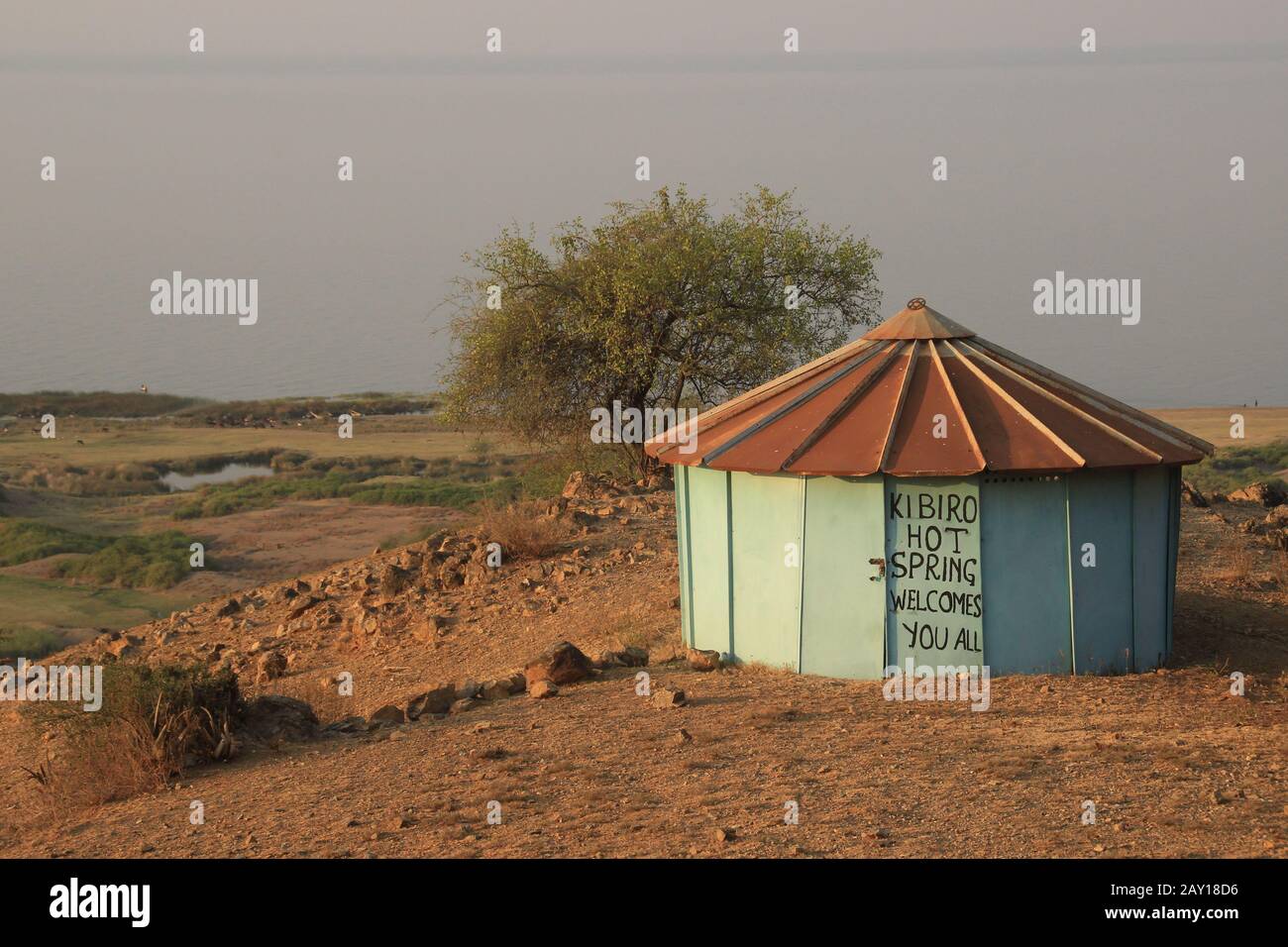 KIBIRO, UGANDA - 17. FEBRUAR 2015: Eine arme afrikanische Hütte in der Savanne mit einem Willkommensschild - eine wenig bekannte Attraktion sind die heißen Quellen in Uganda. Stockfoto