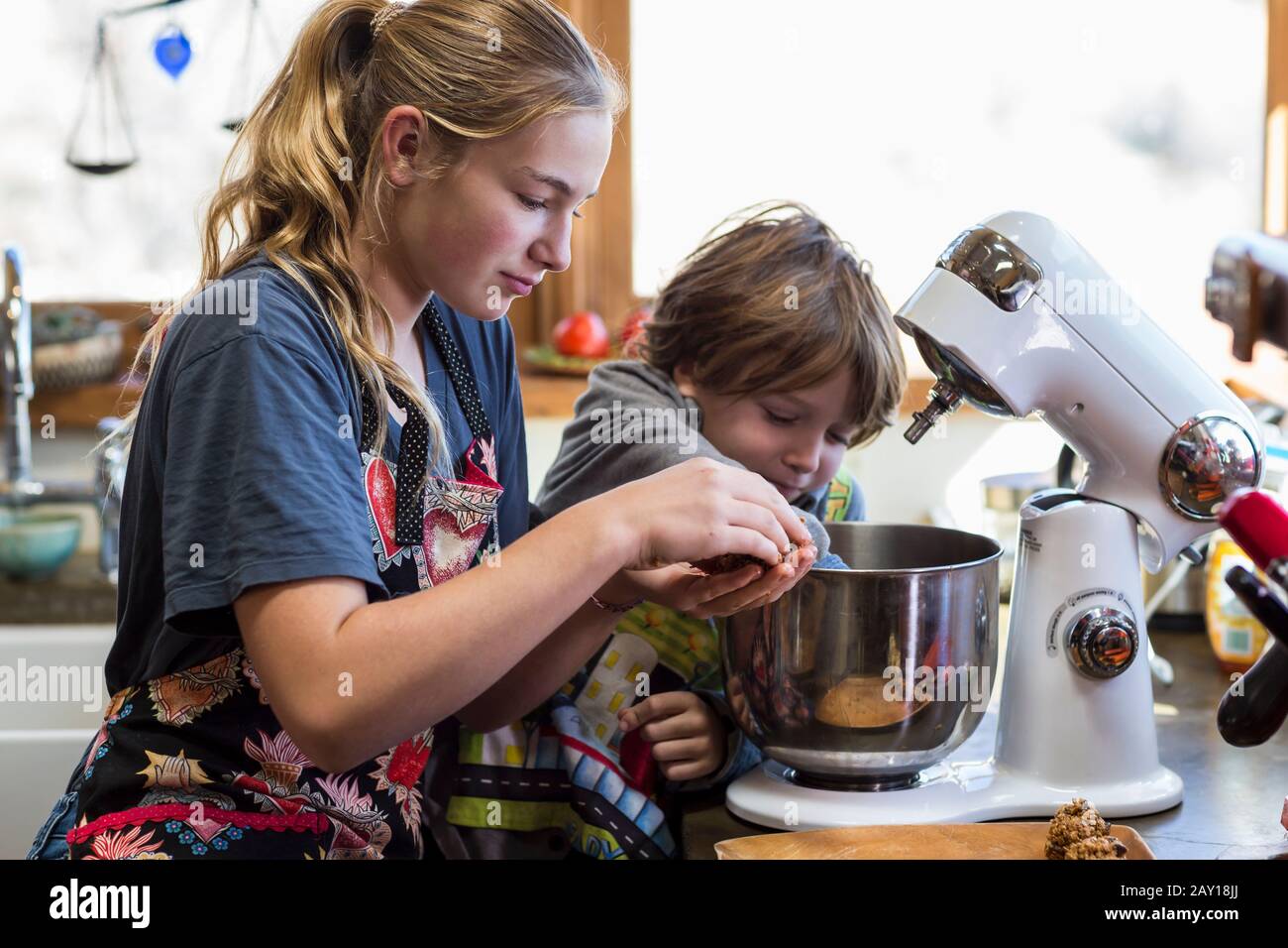 Das dreizehnjährige Mädchen im Teenager-Alter und ihr Bruder im Alter von 6 Jahren in der Küche mit einer Mischschale Stockfoto
