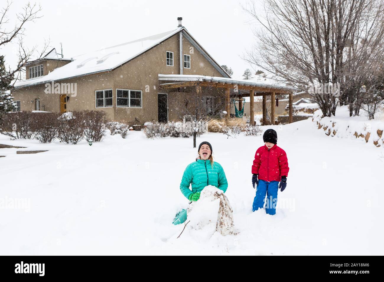 Zwei Kinder in warmer Kleidung im Tiefschnee, die einen Schneemann bauen Stockfoto